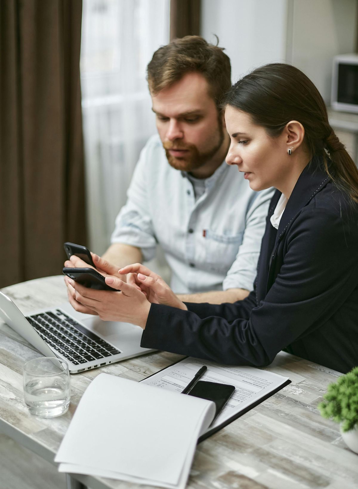 Consultant et consultante analysant un dossier sur téléphone et ordinateur, illustrant l'accompagnement VAE proposé par les 2 Rives pour les partenaires